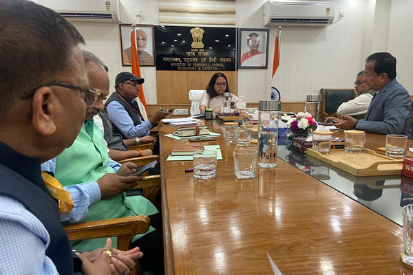 A woman leads a meeting with men in attendance around a table.